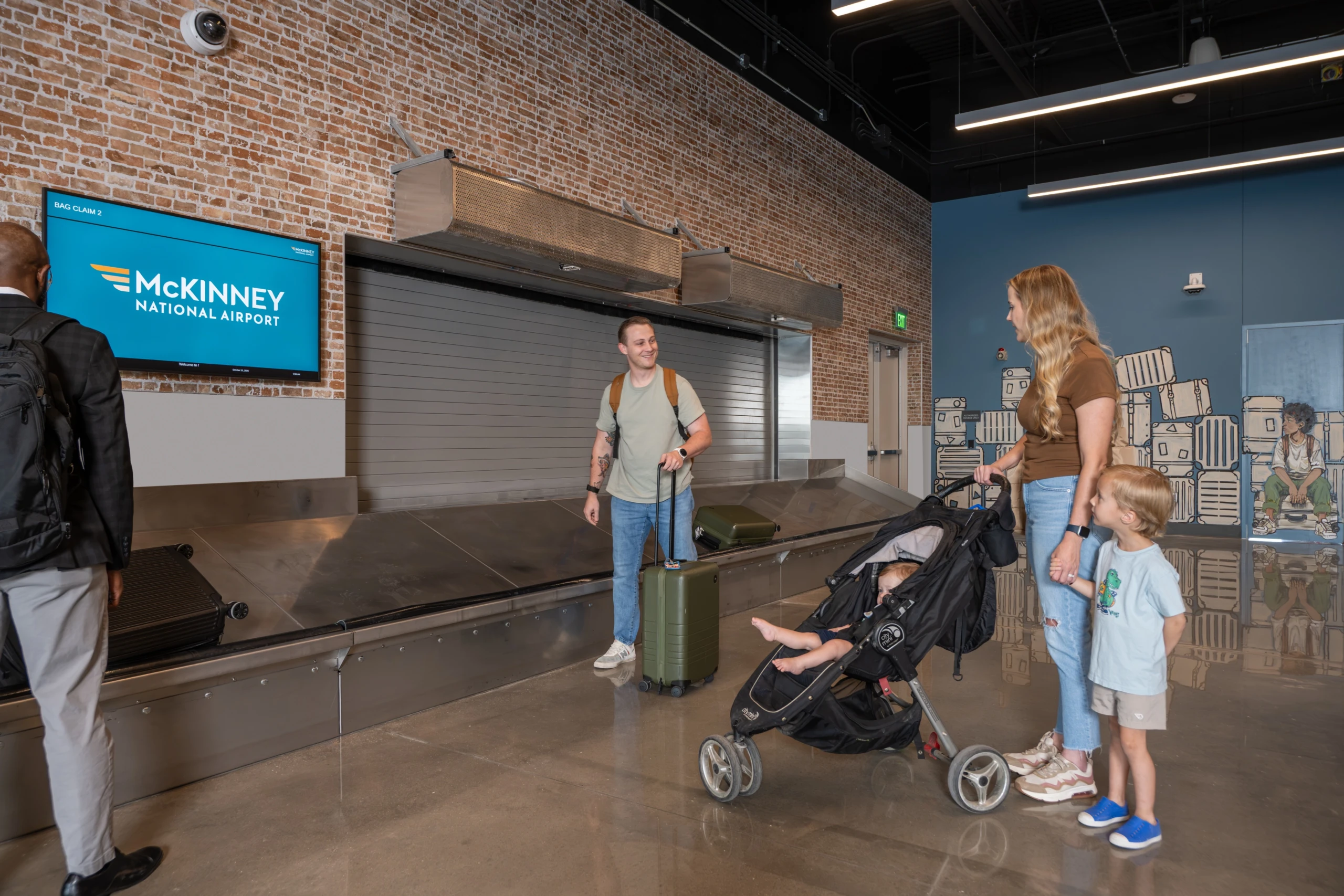 Travelers with a stroller and luggage at the baggage claim carousel, under a McKinney National Airport screen.