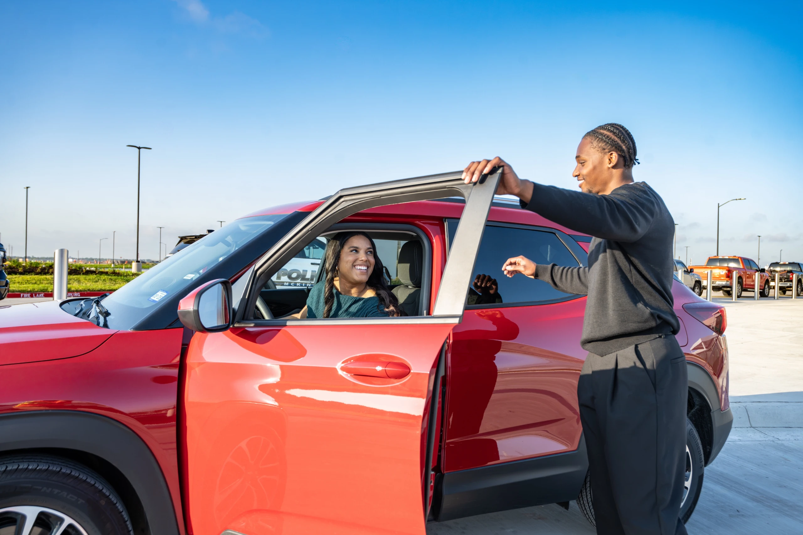 A smiling driver takes the keys to a red rental car from an agent.