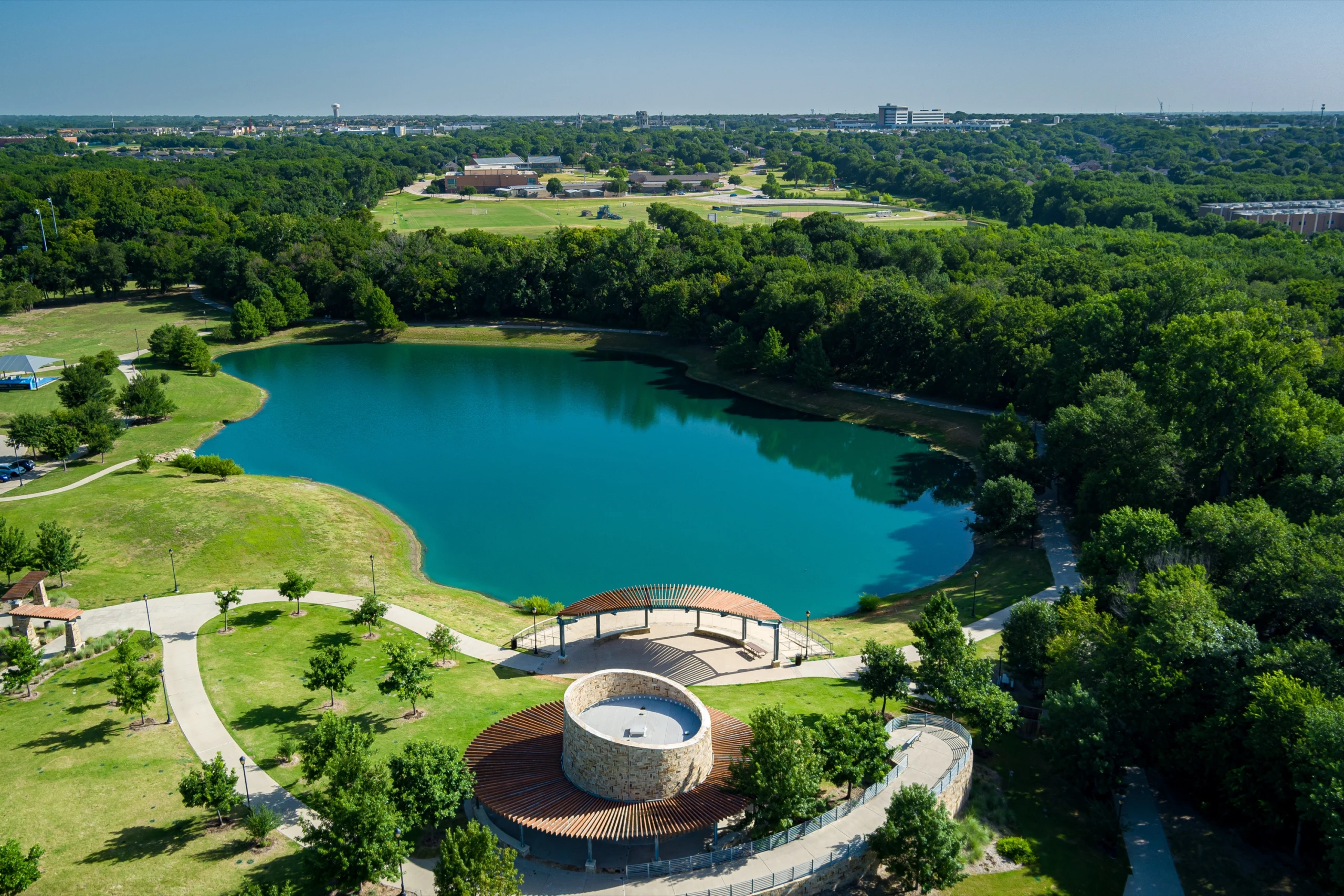 Bonnie Wenk Park from the air: a lake, a curved amphitheater and walking paths among the trees.