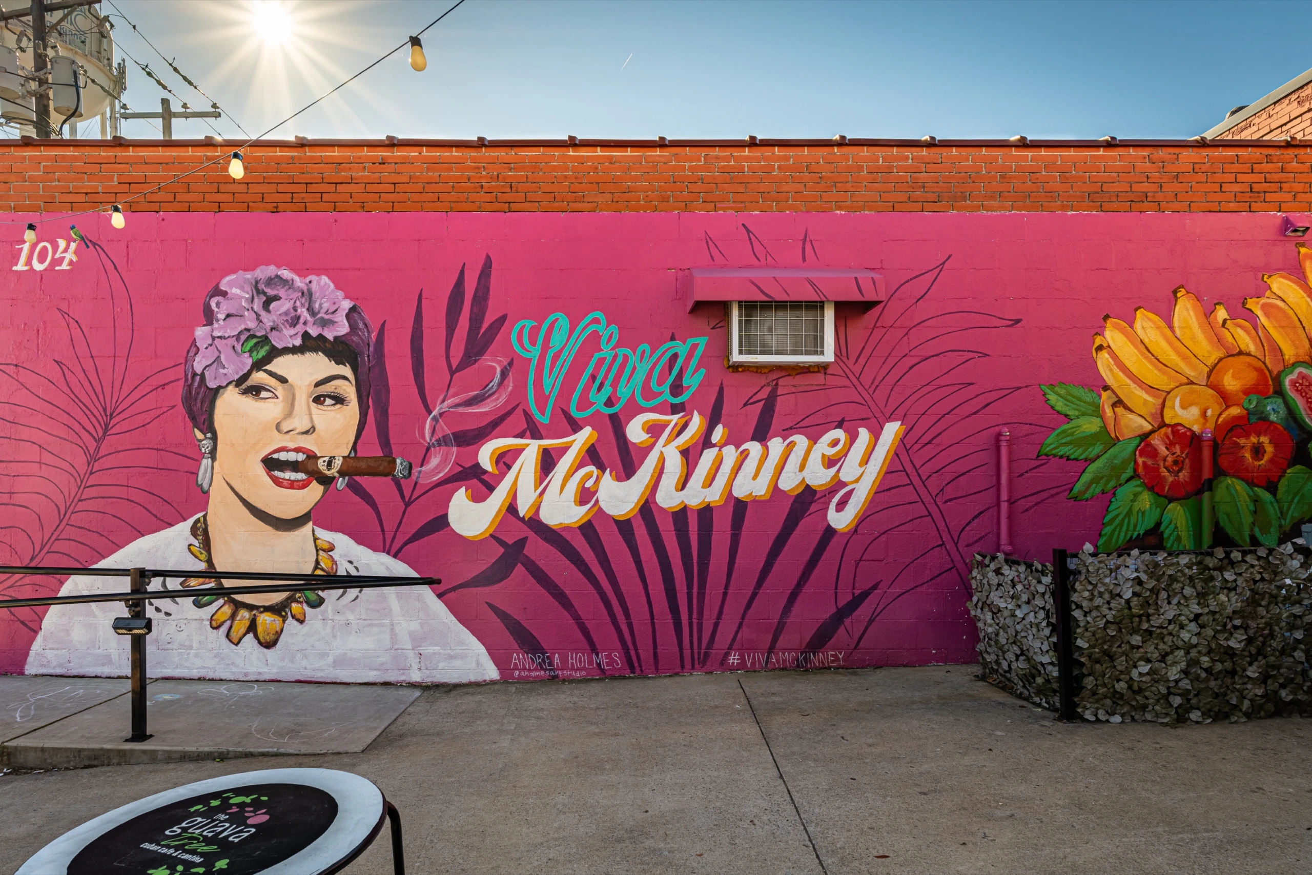 A pink mural reading “Viva McKinney”, with a painted portrait of a woman in a flower crown and a pile of tropical fruit.