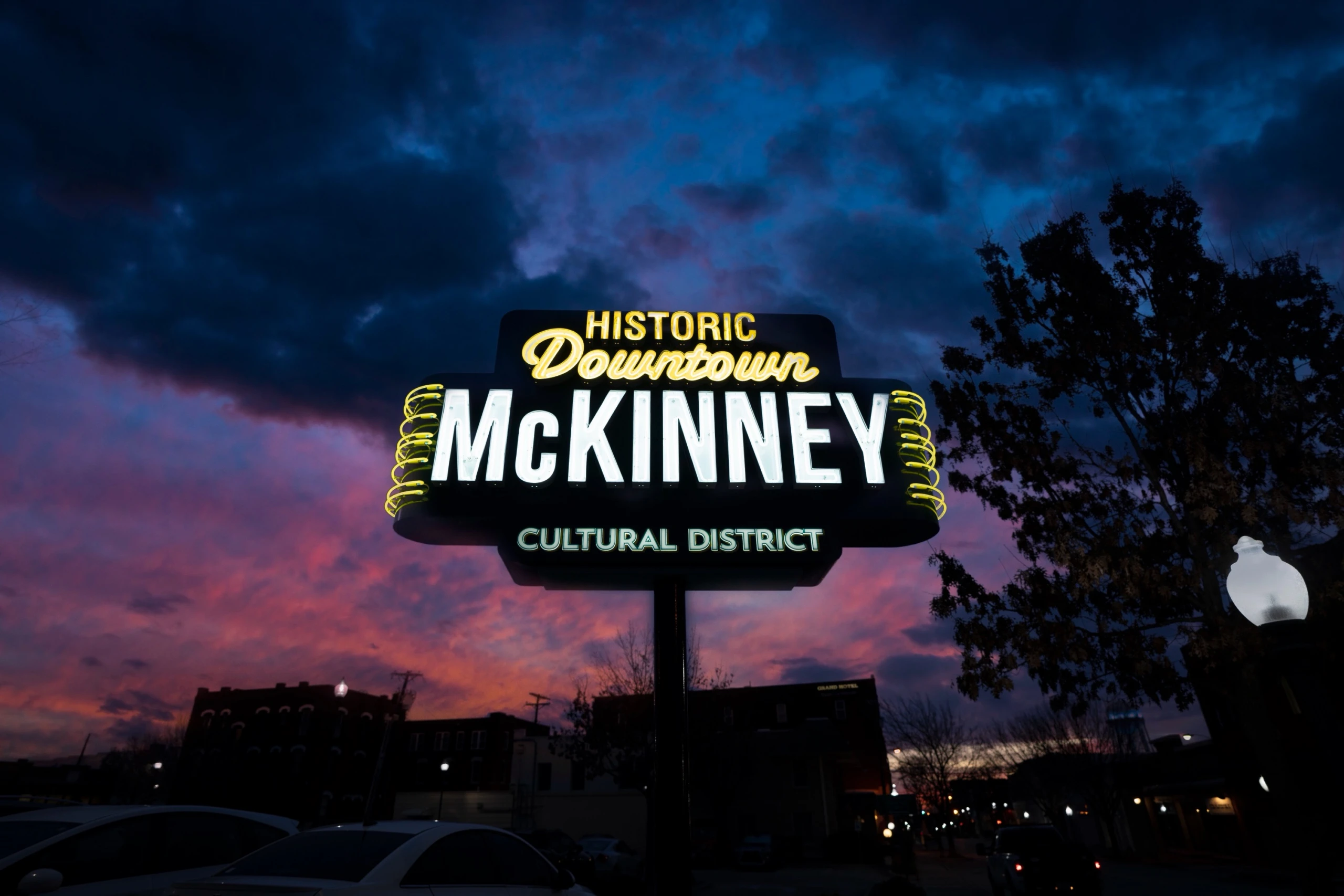The lit neon sign for the Historic Downtown McKinney Cultural District against a purple and pink dusk sky.