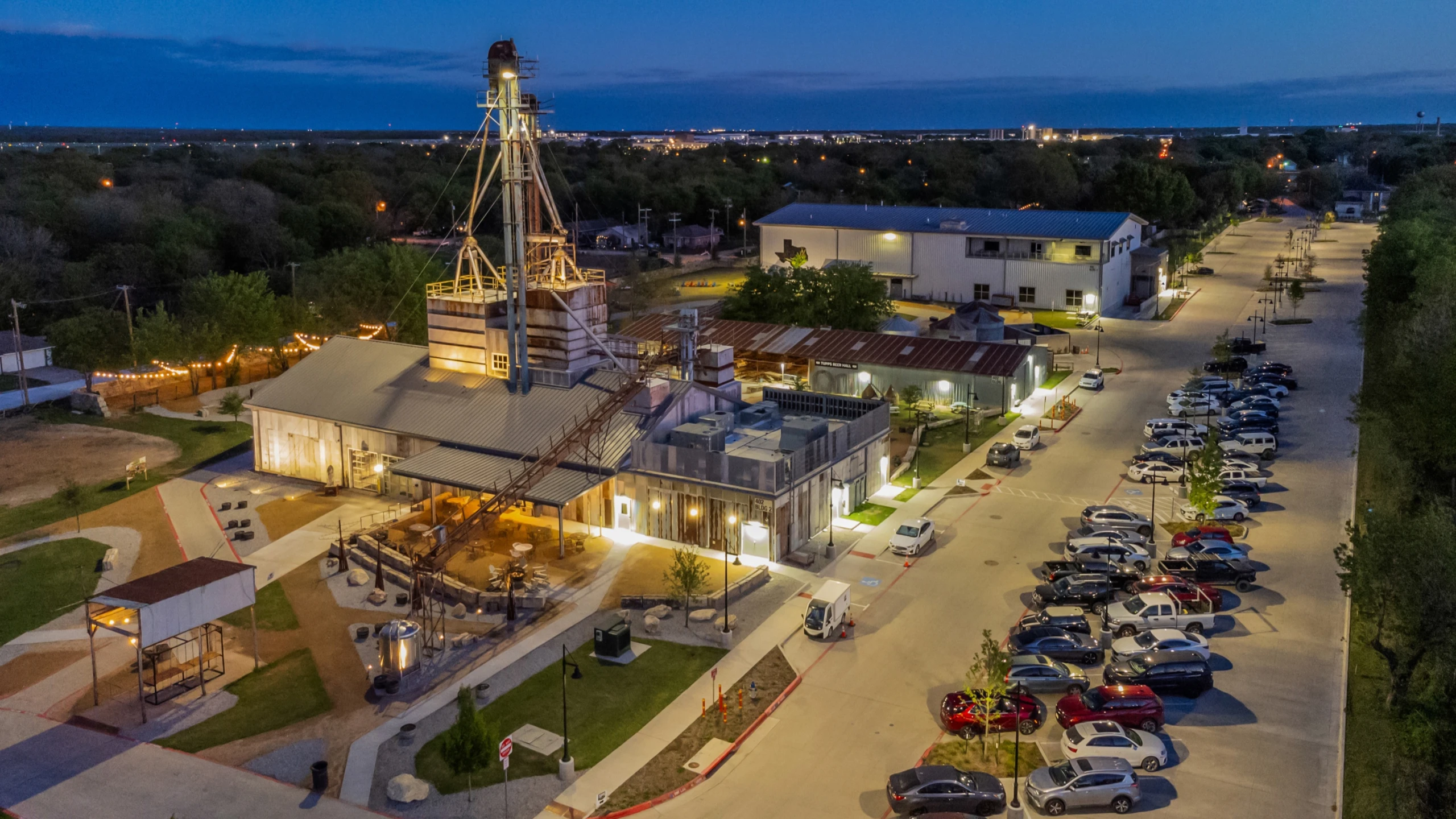 The Tupps Brewery campus in McKinney at dusk, its grain elevator and buildings lit up.